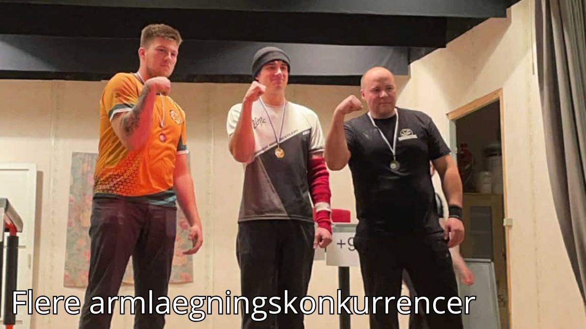 Billedet viser tre mænd, der står på en præmiescene med medaljer om halsen efter en armlægningskonkurrence. De poserer stolt med knyttede næver som et symbol på deres præstationer. Baggrunden er en enkel indendørs opsætning, der fremhæver fokus på deltagerne. Billedetekst: "Flere armlægningskonkurrencer.