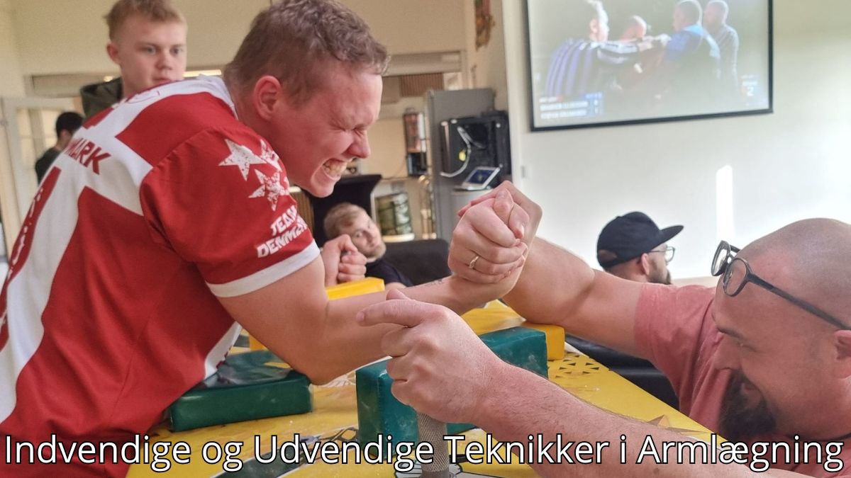 Billedet viser to mænd engageret i en armlægningsduel. Den ene mand, iført en rød trøje med "Team Danmark," udstråler intens koncentration og styrke, mens han kæmper mod en modstander med briller. Baggrunden inkluderer tilskuere og en skærm, der viser en armlægningskamp, hvilket giver en professionel atmosfære. Billedetekst: "Indvendige og Udvendige Teknikker i Armlægning''