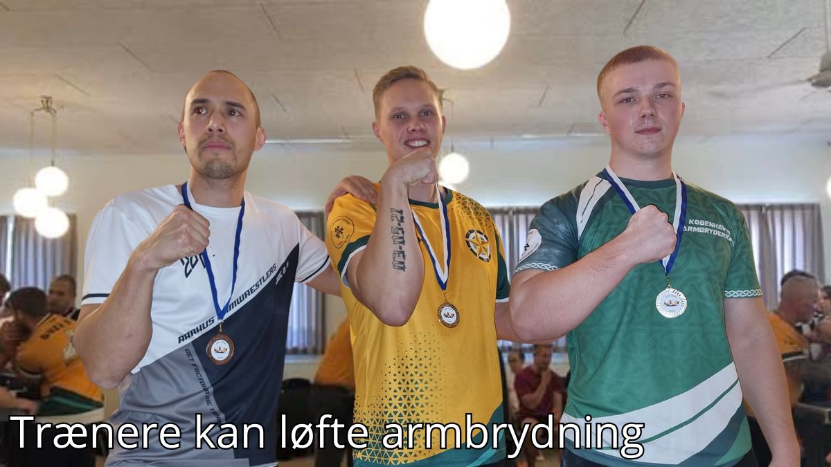 Billedet viser tre mænd iført holdspecifikke trøjer, der stolt fremviser deres medaljer og poserer med hænderne knyttet i en sejrspositur. Baggrunden viser en indendørs hal med andre deltagere og tilskuere, hvilket skaber en stemning af konkurrence og fællesskab. Billedetekst: "Trænere kan løfte armbrydning''